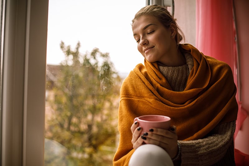 5 Tips to Improve Your Indoor Air Quality This Fall. A woman enjoying fall weather with a cup of coffee.